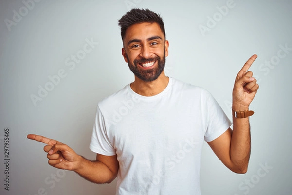 Fototapeta Young indian man wearing t-shirt standing over isolated white background smiling confident pointing with fingers to different directions. Copy space for advertisement