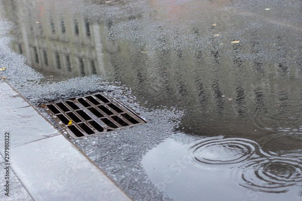 Fototapeta Autumn asphalt, metal grating stormwater on a city street. Autumn rainy weather with puddles, outflow of water from the highway. backdrop texture background