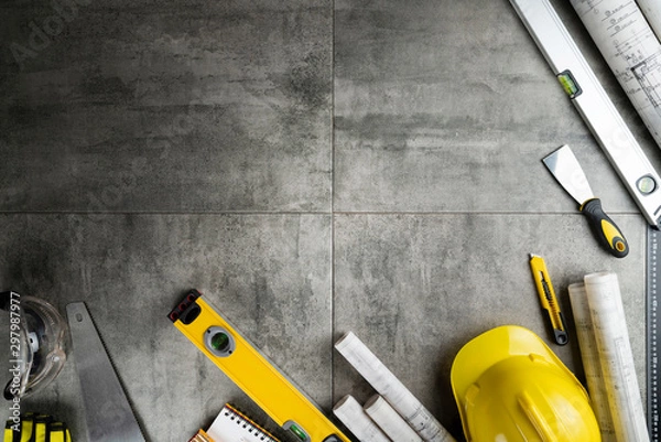 Fototapeta Contractor concept. Yellow hardhat, libella and plans on the gray tiles.