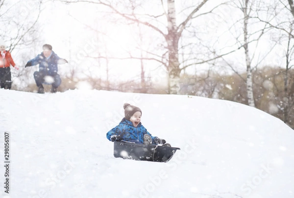 Fototapeta Children in the park in winter. Kids play with snow on the playground. They sculpt snowmen and slide down the hills.