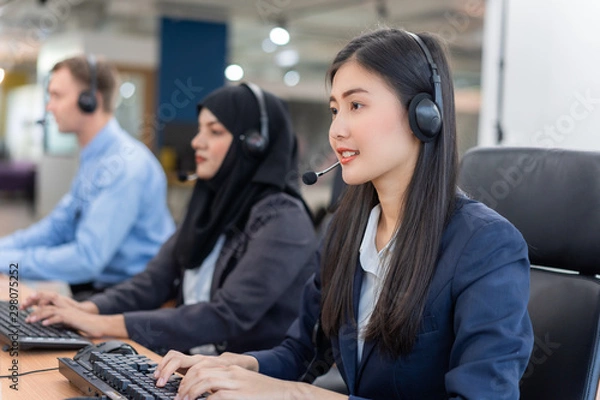 Fototapeta Happy smiling operator asian woman customer service agent with headsets working on computer in a call center, talking with customer for assisting to resolve the problem with her service mind