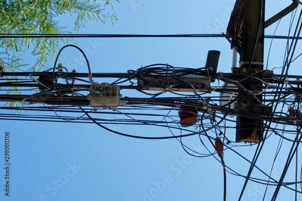 Fototapeta Tangled and messy of electric wires on electric pole in the city with sky background.