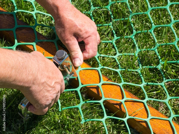 Fototapeta fastening plastic mesh to wooden racks with a stapler