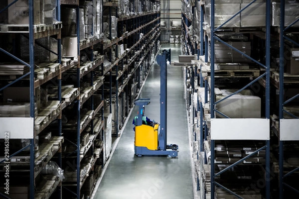 Obraz yellow electric forklift reach truck in a warehouse pulls out a pallet from a high shelf against the background of a discolored warehouse
