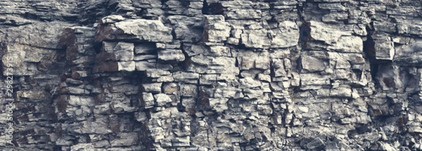 Fototapeta Dangerous vertical wall with protruding crumbling layered wild stone blocks. Rock cliff face background. Toned. Abstract texture for stone mining industry. Copy space for custom text