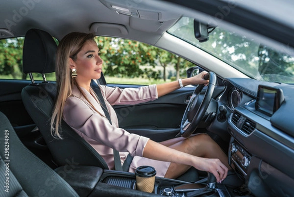Obraz Beautiful girl business lady summer city car. Reversing, looking rearview mirror, engaging reverse gear, traffic jam parking lot. Car rental, car sharing. Automatic transmission. Autumn day nature.