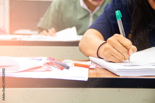 Fototapeta University students do quiz, test or studies from the teacher in a large lecture room. Students in uniform attending exam classroom educational school.
