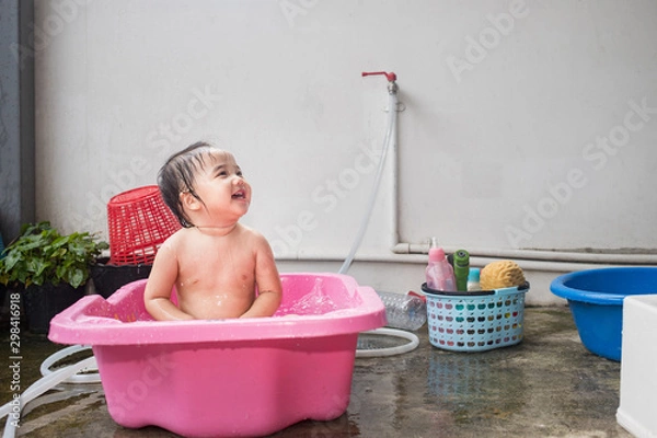 Fototapeta Baby kid taking a bath in pink bathtub and making water splash