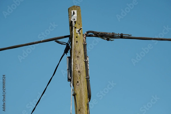 Fototapeta Newly installed power cables seen attached to a very old wooden telegraph pole in a village location.