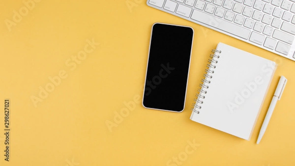 Fototapeta Flat lay design of modern office table with smartphone, laptop, notebook and pen on yellow background with copy space. Top view. Business, Workspace, learning and education concept.