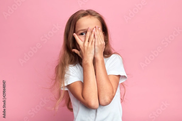 Fototapeta emocjonalna mała dziewczynka zakrywa twarz ręką odizolowaną na różowym tle, dziecko ogląda horror, film, reakcję, wyraz twarzy. pojedyncze różowe tło