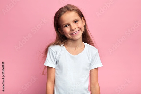 Fototapeta cheerful blonde girl in white T-shirt looking at the camera with positive expression. close up portrait, isolated pink background, studio shot