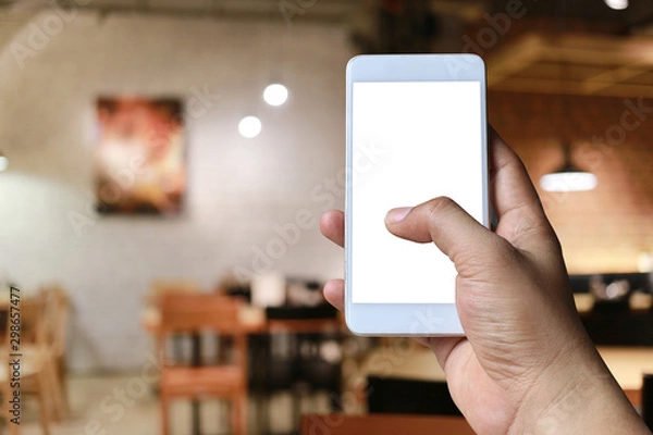 Fototapeta Hand of a man holding smart phone device in the coffee cafe background.