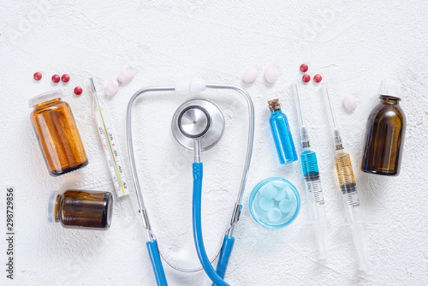 Fototapeta Syringe, stethoscope, thermometer, various tablets and bottle with blue liquid on a white background. Medical flat lay background.