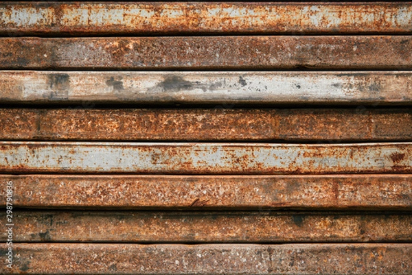 Fototapeta Racks of metal profiles. Metal is stored in an open warehouse. Wet and rusty on the street. Old grunge background made of rusty iron for shooting flatleys on the table. Copy space