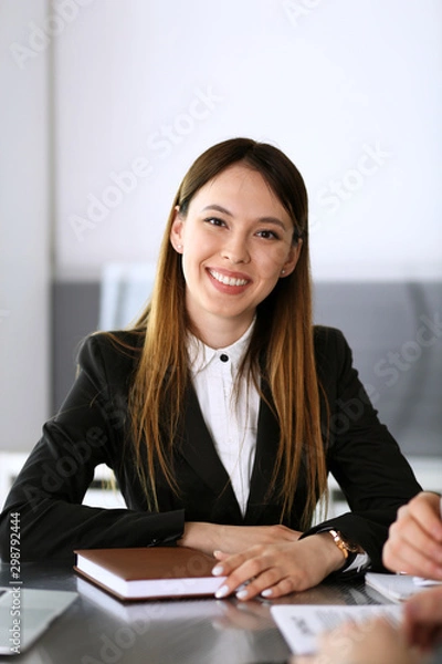 Fototapeta Happy smiling business woman headshot. Unknown businesswoman sitting at meeting or negotiation in modern office with colleagues at the background. Teamwork and partnership concept