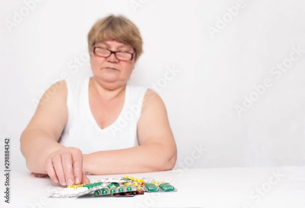 Obraz Elderly woman chooses a tablet on the table. The concept of self-medication and side effects of pills, copy space