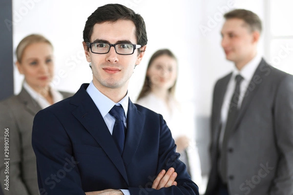 Fototapeta Headshot of businessman standing straight with colleagues at background in office. Group of business people discussing questions at conference or presentation. Success and business concept