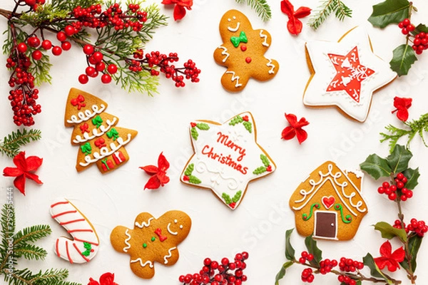 Fototapeta Christmas background with gingerbread cookies and branches of holly with red berries on white. Winter festive nature concept. Flat lay, copy space.