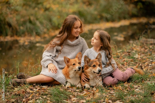 Obraz two sisters sitting on the ground with dogs in the autumn park