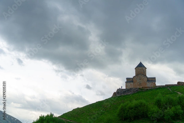 Fototapeta Gergeti Trinity Church also known as Tsminda Sameba on the background of a mountain ridge and clouds, Stepantsminda, Kazbegi