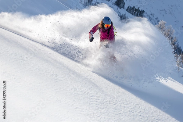 Fototapeta Snowboardzistka zakrzywiała się i hamowała rozpylając luźny, głęboki śnieg na stoku freeride. zjazd z deskami snowboardowymi w świeżym śniegu. mistrz świata we freeride. wiry śniegu w powietrzu, w jasnej masce