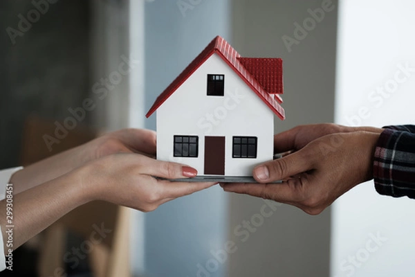 Fototapeta Real estate agent holding house model and pass to customer, Property concept.