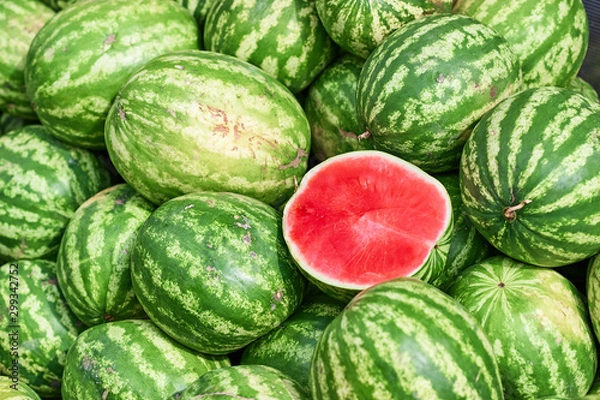 Obraz A total plan of a pile of watermelons on which lies the cut half of the watermelon. Half of the watermelon pitted ready for sale. Trade watermelons outdoors.