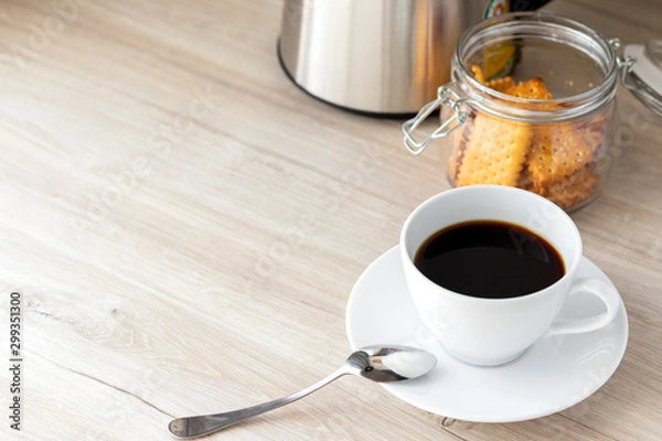 Fototapeta Coffee in a cup on the table and cookies in a glass jar and kettle, morning drink, breakfast, copy space.