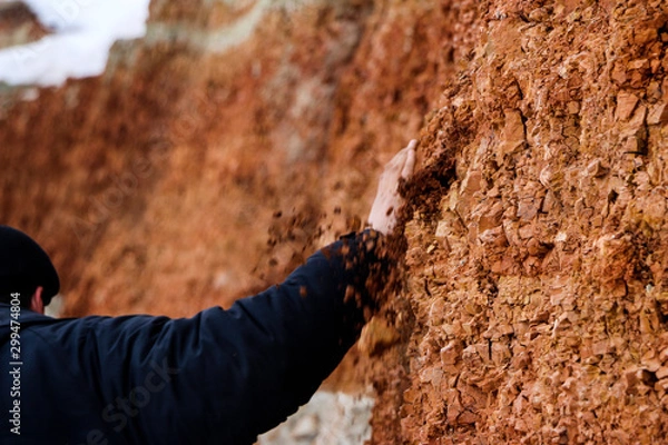 Fototapeta young man walks in  clay career in winter.  guy touches his hands with multi-colored layers of clay in  excavation.