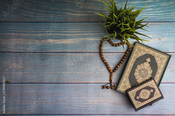 Obraz Flat lay view of vase, tasbih or rosary beads and Holy book of Quran with arabic calligraphy meaning of Al Quran over wooden paper background. Selective focus and crop fragment