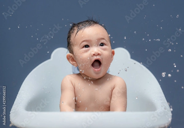 Fototapeta Cute baby boy bathes in a bathtub play and making splash water drops, smiling cheerful. Concepts for health care and daily routine.
