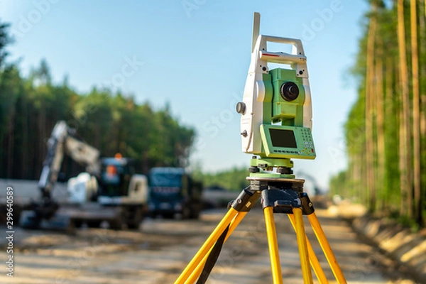 Fototapeta Surveyor engineer with equipment (theodolite or total positioning station) on the construction site of the road or building with construction machinery background