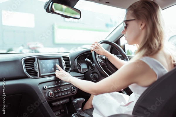 Obraz woman driving car, presses finger on touch screen, selects application on Internet, activates radio navigation and searches for route in the city. Background parking mall.