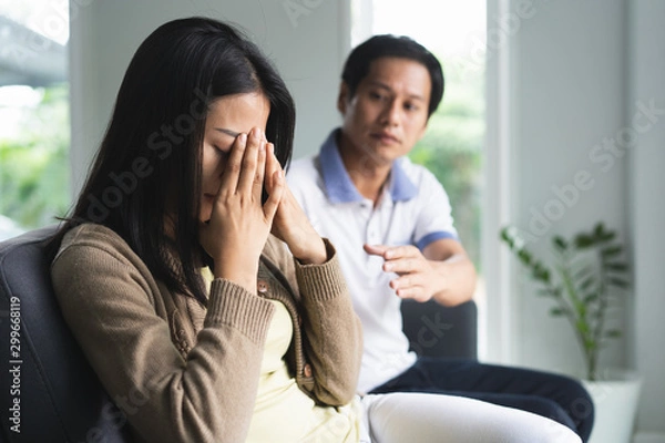 Fototapeta Asian couple having relation problem. Wife crying and sitting separate with her husband at home after quarrel.