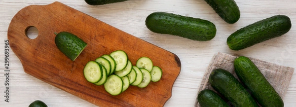 Fototapeta Fresh organic mini baby cucumbers on a rustic board on a white wooden surface, top view. Flat lay, from above, overhead.