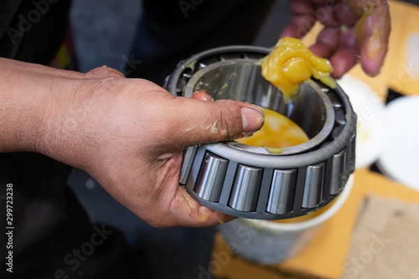 Obraz Senior worker putting lubricant lithium grease (NLGI 3) into wheel bearing for ten wheel truck car by hand at service station in Asia. Grease appearance is yellow. Maintenance and preventive concept. 
