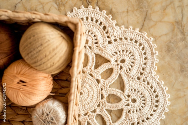 Obraz threads, crocheted round napkin. White napkin like a flower. on a marble light background. Balls of thread in a wicker box.cozy home and handmade concept