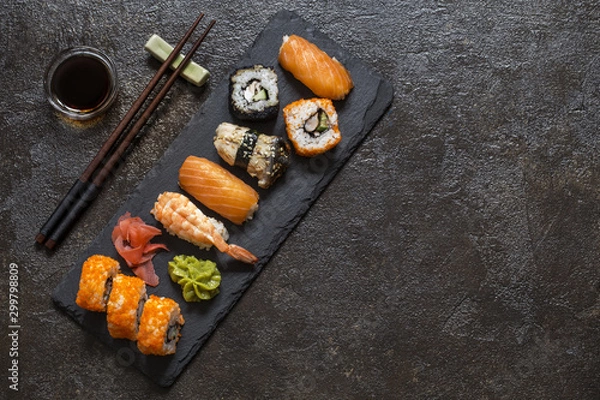 Fototapeta sushi rolls with rice and fish, soy sauce on a dark stone background
