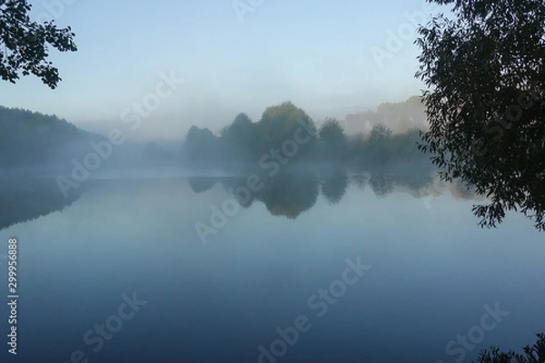 Obraz Early morning on the lake. Fog above the water. The shore is covered with trees.
