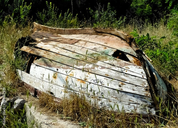 Fototapeta Derelict overturned wooden rowing boat hull. Weather beaten, with broken & holed planking. Paint peeling with visible graining.  Overturned in overgrown raised garden. Lopud, Dalmatia, Croatia, Europe
