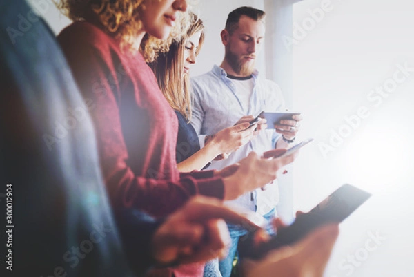 Obraz Team of web designers discussing the bugs of the new internet site while testing usability on the mobile gadgets with different operation systems. Young men and women using mobile internet on gadgets