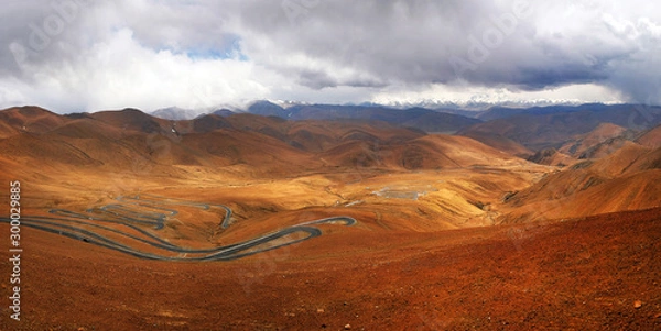 Fototapeta Panoramic view of highway stretching across the brown Himalaya Mountains, against a blue sky covered by white clouds.