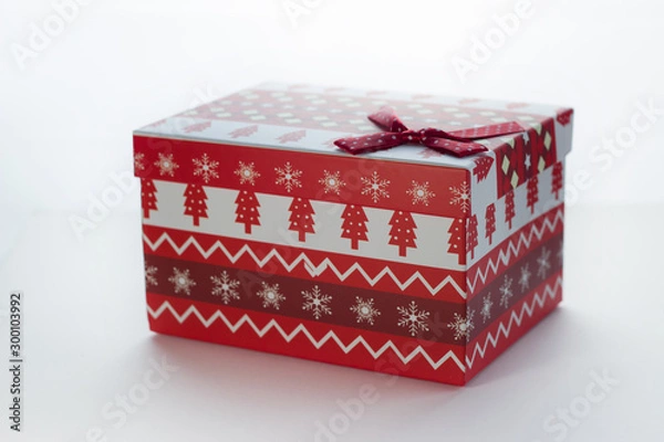 Fototapeta Christmas box with red gifts on white isolated background with the image of Christmas trees close-up angled. There is a bow in the corner