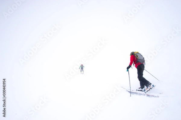 Fototapeta Two skiers struggling into a snow storm during a whiteout in the mountains