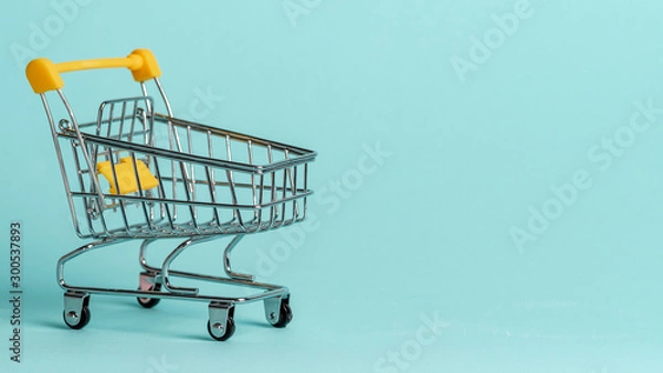 Obraz Shopping cart on blue background. Shop trolley at supermarket as sale, discount, shopaholism concept with copy space for text or design.