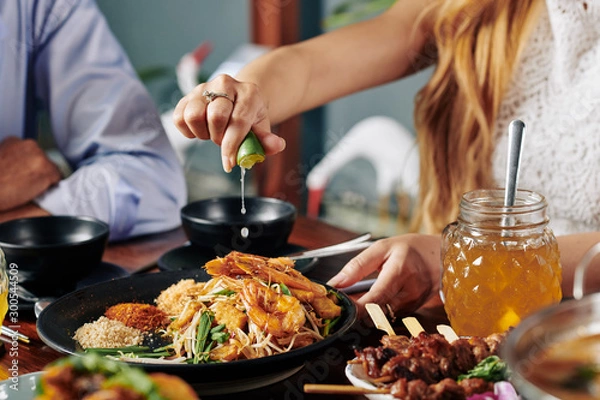 Fototapeta Close-up image of woman squeezing lime in dish with shrimps, sprouts and soba