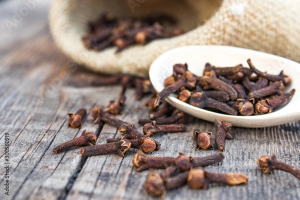 Obraz A spice of dried cloves lies on a wooden spoon and is scattered on old wooden boards near the bag.
