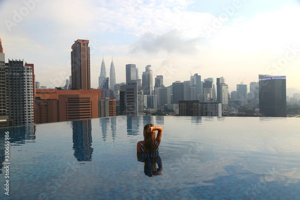 Obraz Young happy girl swimming alone in the infinity pool on rooftop in Kuala Lumpur in Malaysia.