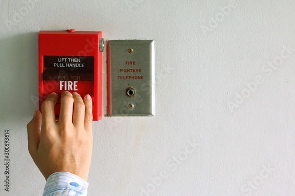 Fototapeta Hand of woman pulling fire alarm switch on the white wall as background for emergency case at the office